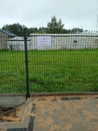 ogrodzenie panelowe, na nim tabliczka z informacją o dofinansowaniu projektu, przed ogrodzeniem chodnik z kostki brukowej,...
