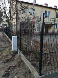 ogrodzenie panelowe, za nim utwardzony plac, budynek, z lewej strony drzewo